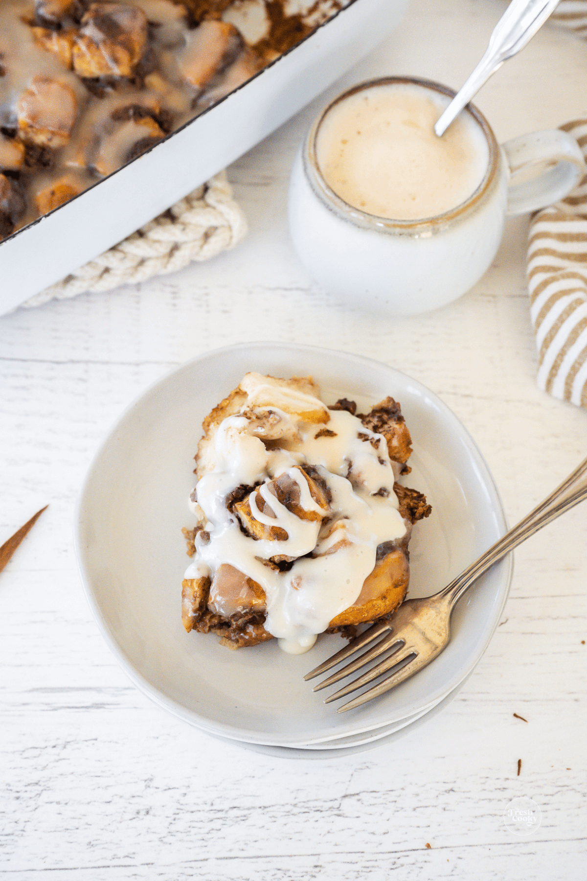 Cinnamon Roll casserole on a plate with a cup of coffee behind.