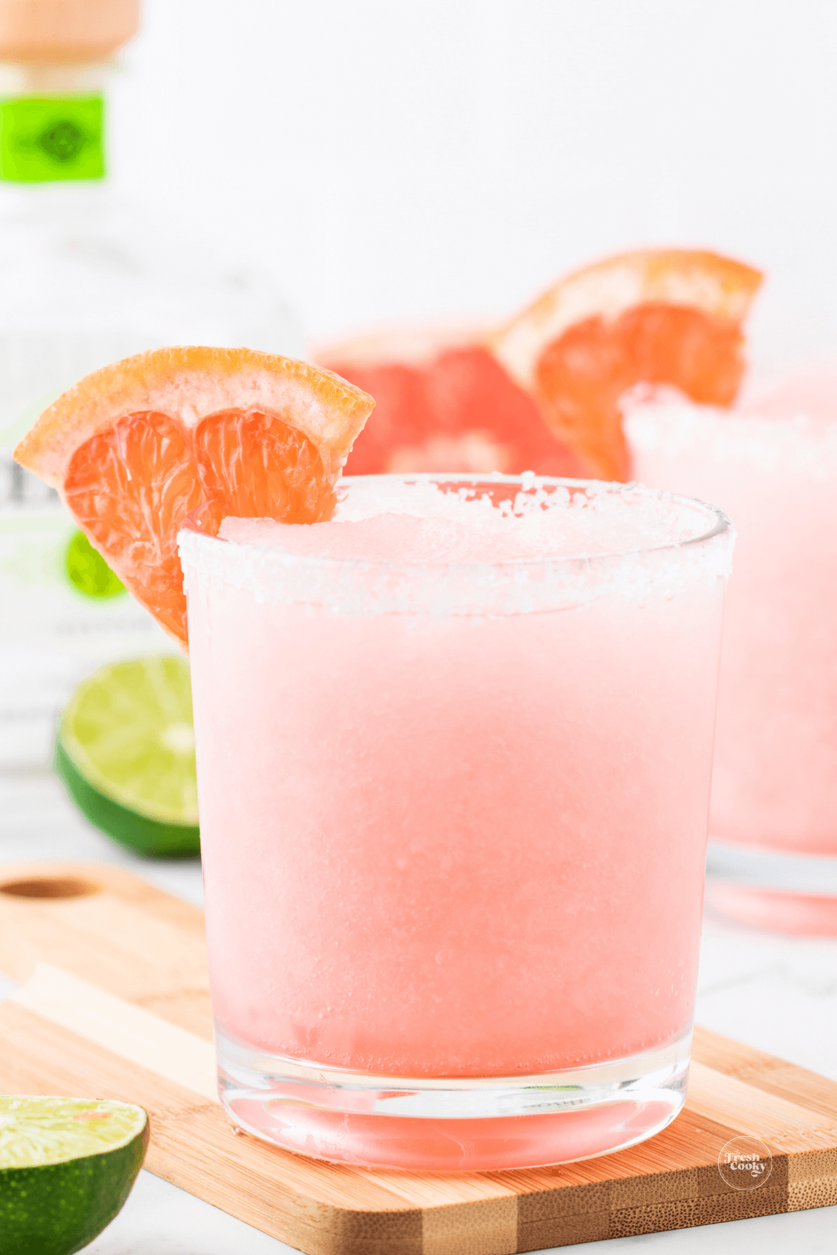 Grapefruit paloma cocktail in glass with tequila bottle behind.