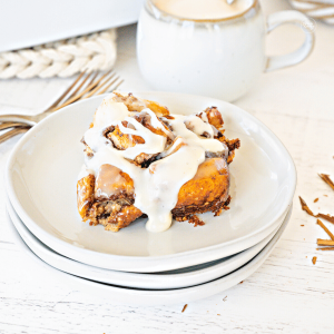 Slice of breakfast cinnamon roll casserole on plates with coffee behind.