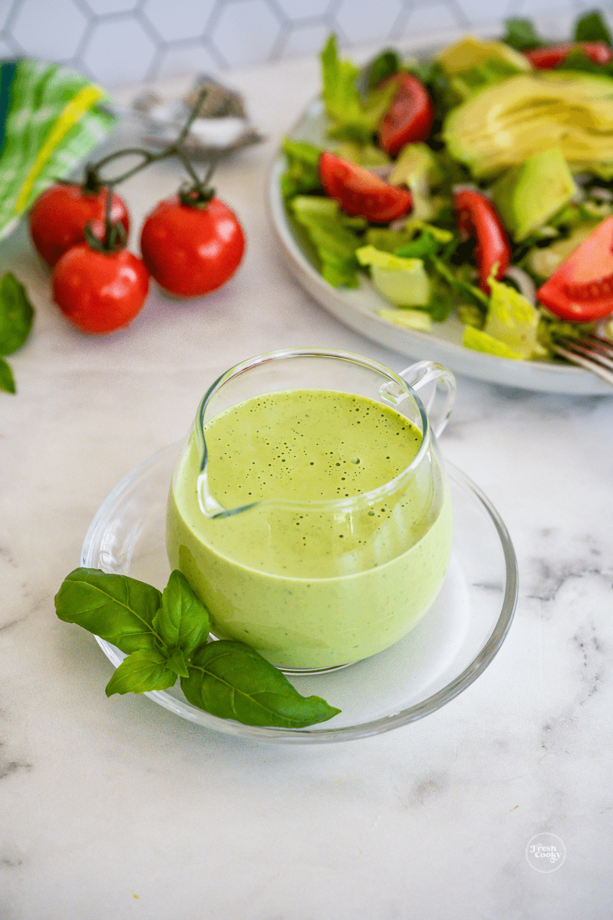 Delicious green goddess dressing in pretty crystal pitcher with green salad behind.