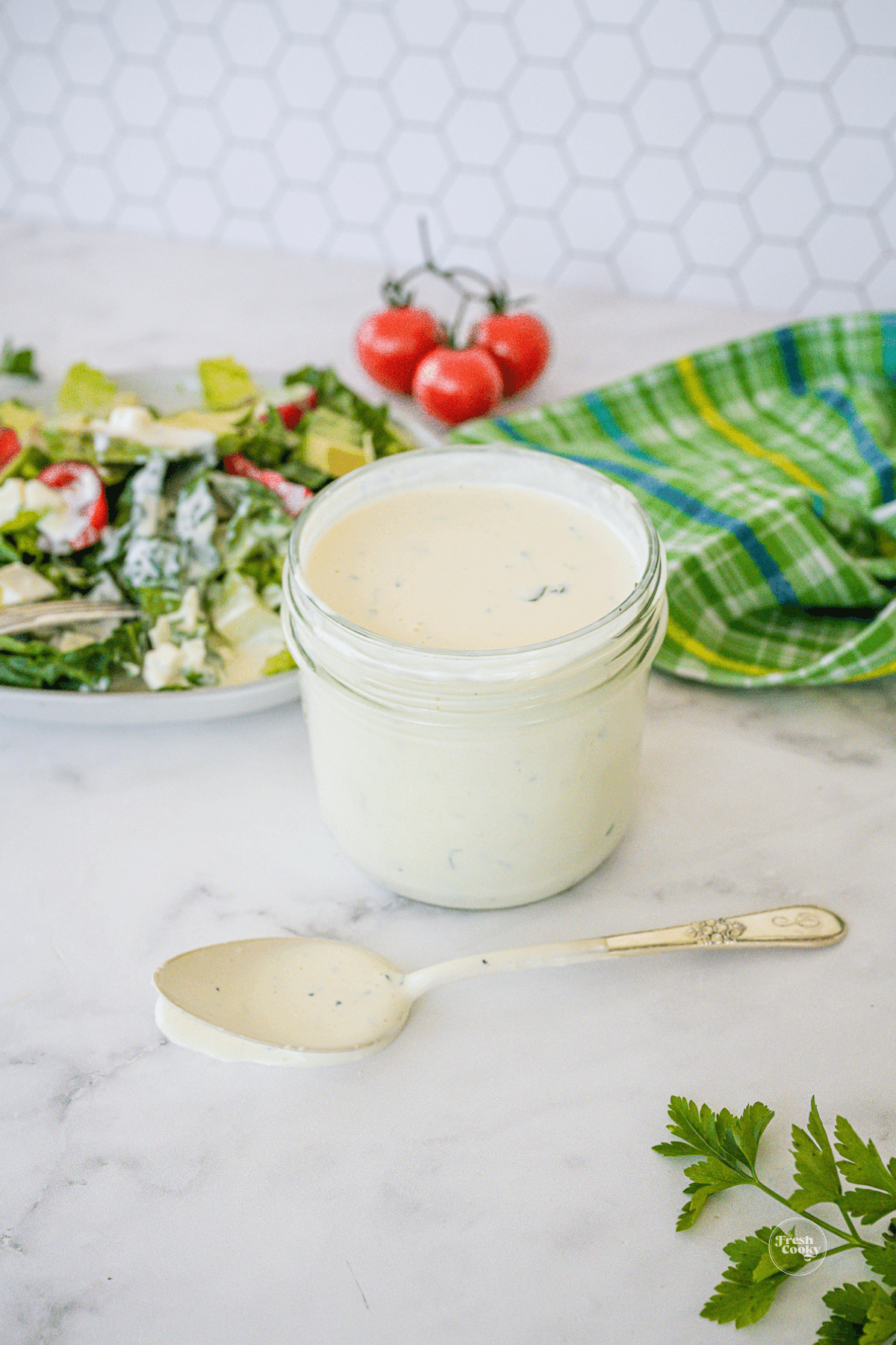 Jar of blue cheese dressing with spoon setting in front and salad in background.