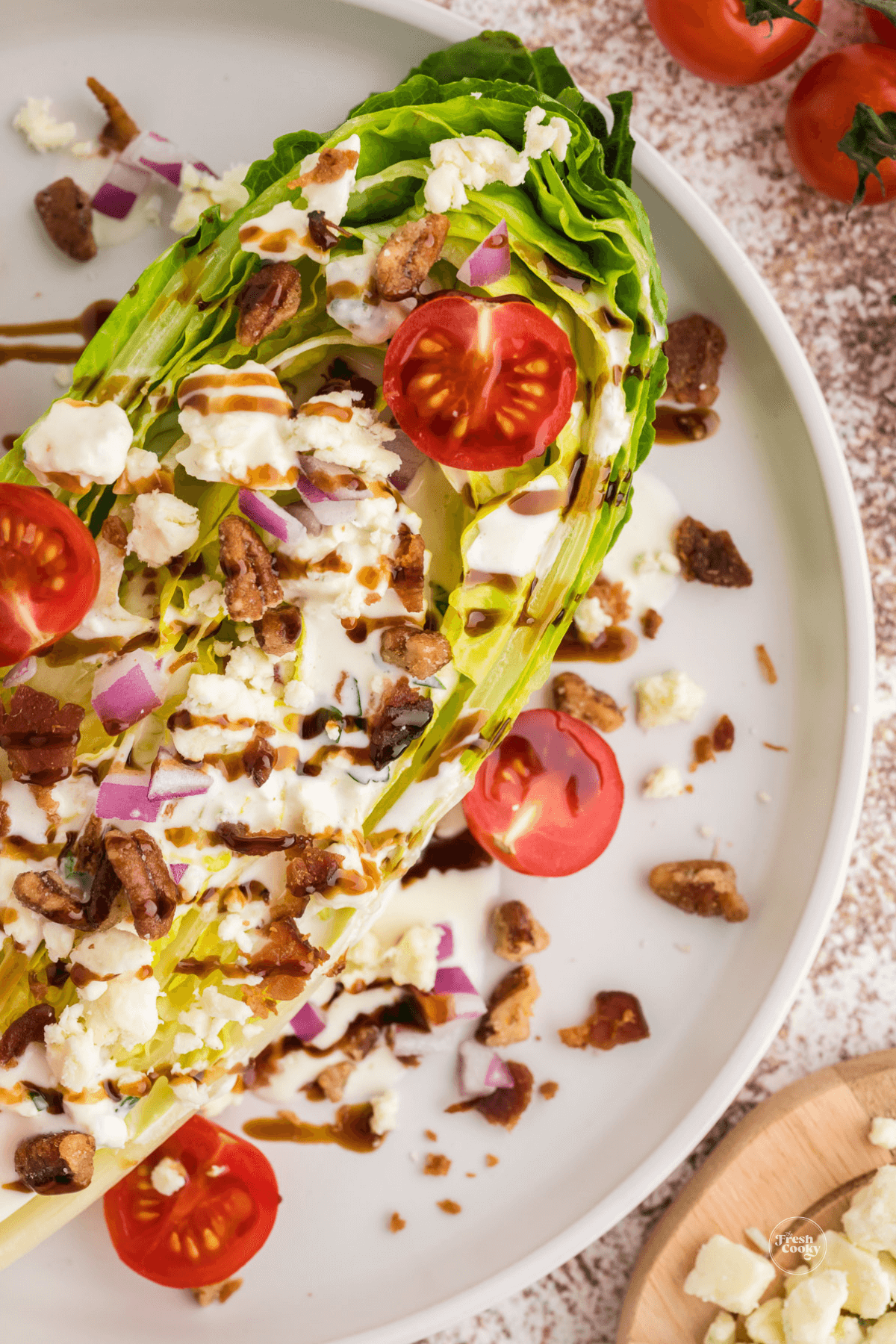 Close up of romaine wedge salad with crispy bacon, red onion, tomatoes, pecans and blue cheese crumbles.