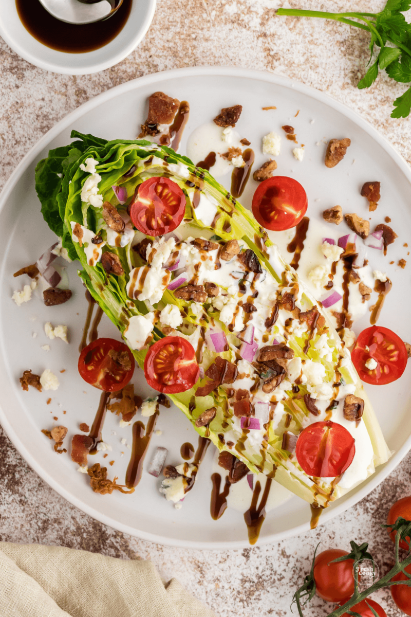 Steakhouse wedge salad drizzled with balsamic glaze, blue cheese crumbles, halved tomatoes, bacon bits and pecans. 