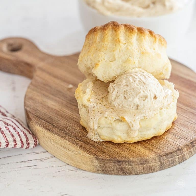 Fluffy biscuit with cinnamon honey butter melting onto small cutting board.