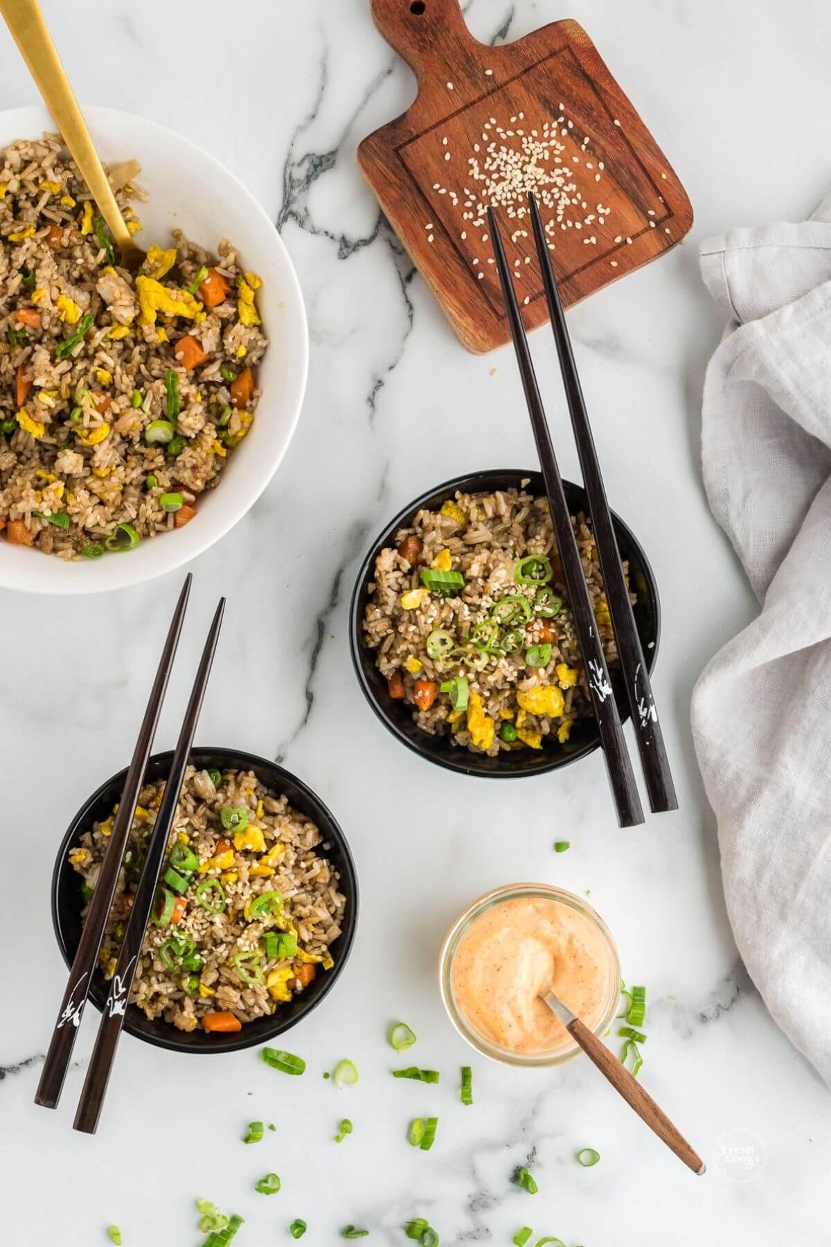 Serving bowls with hibachi fried rice with chopsticks resting on top, yum yum sauce included.