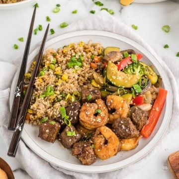 Plate filled with tender steak and shrimp, with fried rice and hibachi vegetables with chopsticks.