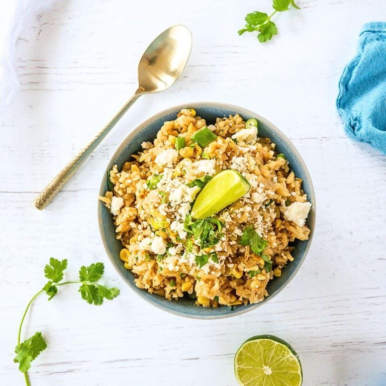 Mexican corn rice recipe in a bowl garnished with lime, cilantro and cotija cheese.