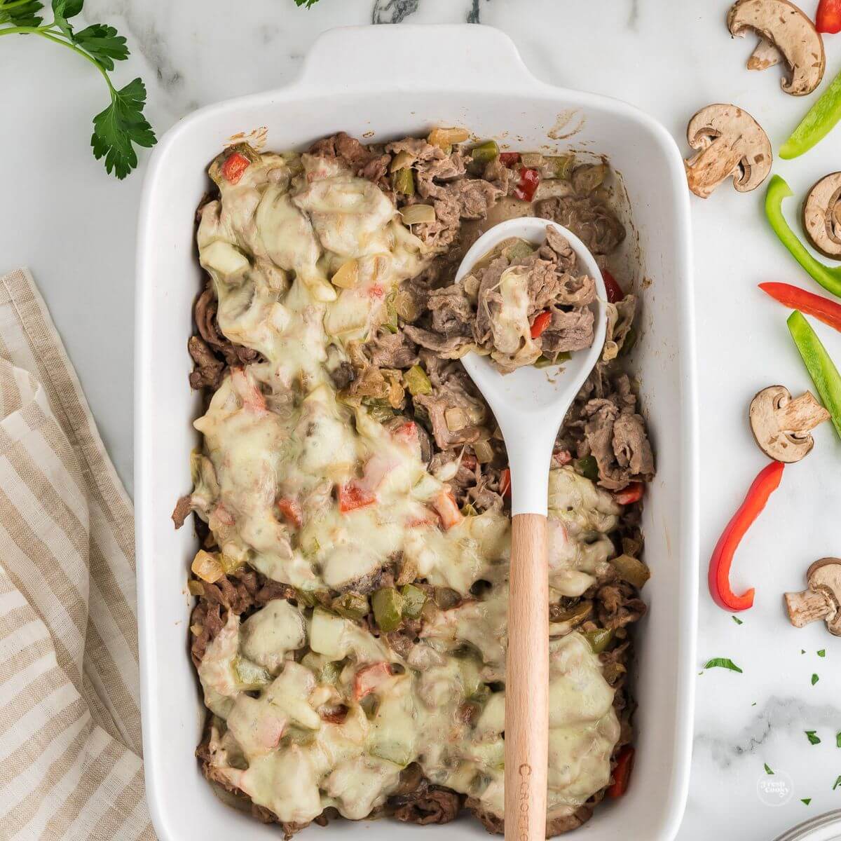 Philly cheesesteak casserole recipe with serving spoon in casserole dish.