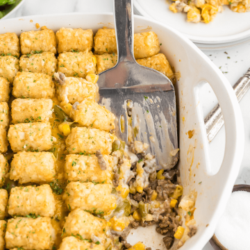 Cheesy hamburger tater tot casserole recipe with spatula spooning out a serving.