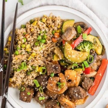 Hibachi steak, shrimp with fried rice, and hibachi veggies on plate with chopsticks.