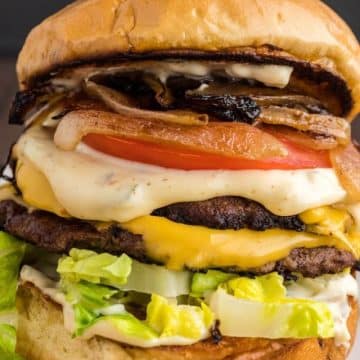 Close up of double smashburger with cheese, layered with grilled onions, smash sauce, lettuce and tomato.