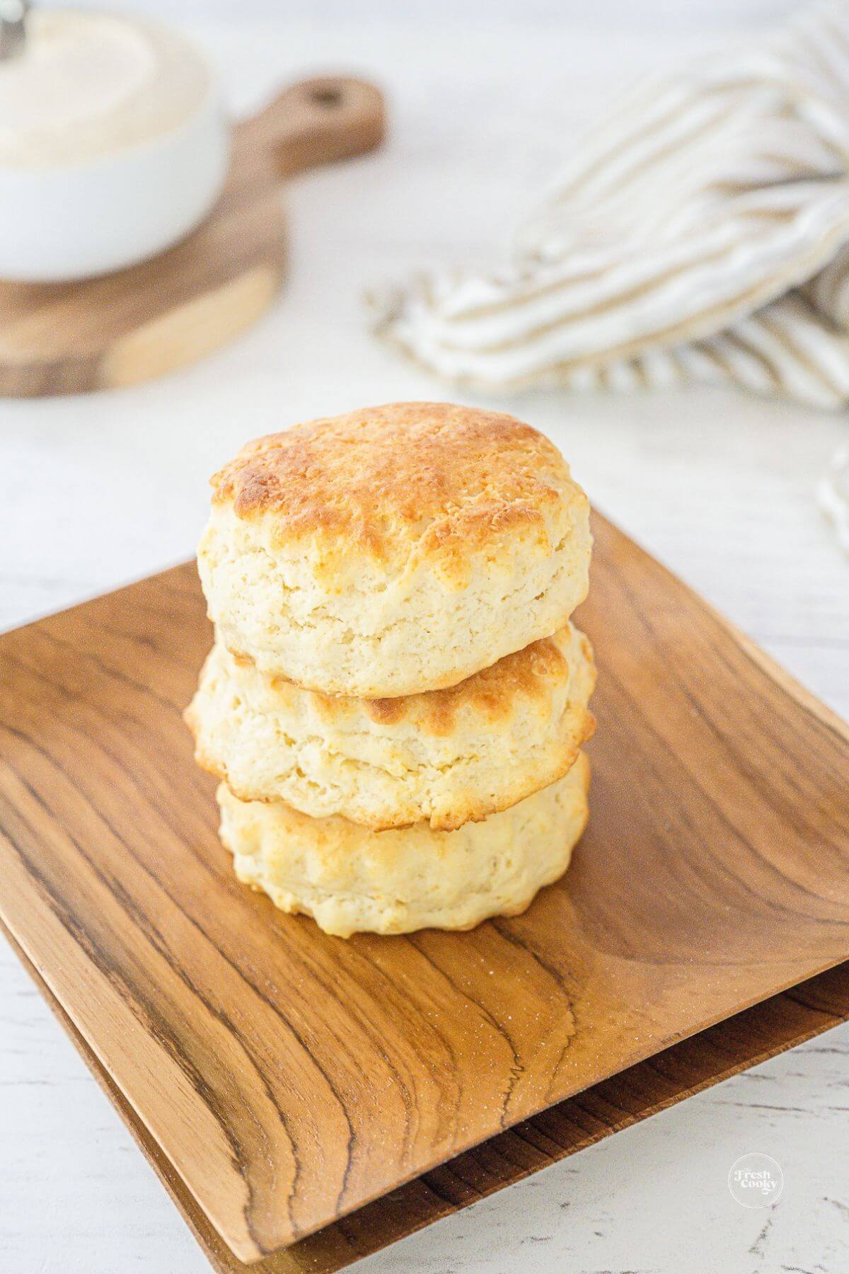 Stack of easy homemade biscuits on wooden plates with honey butter in background.