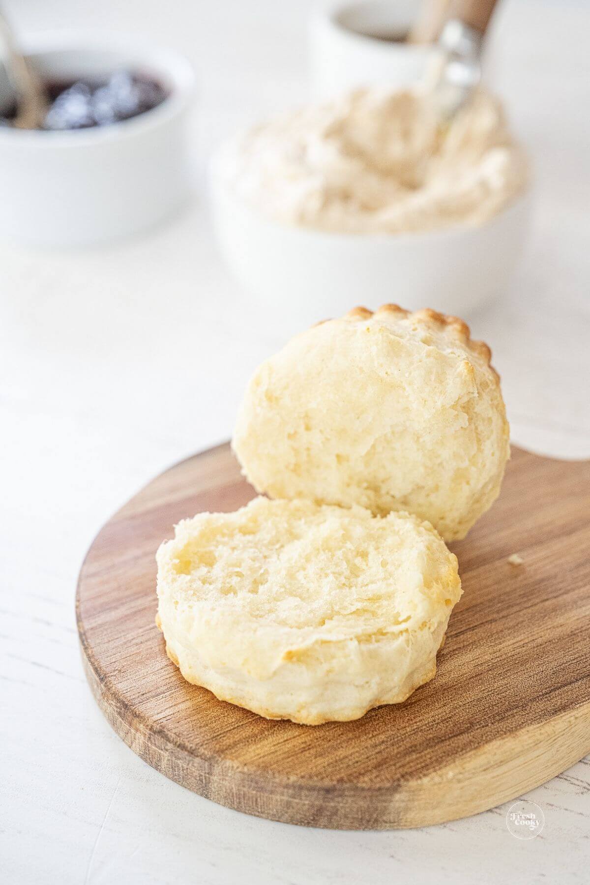 Tall biscuit, split in half with honey butter in background.