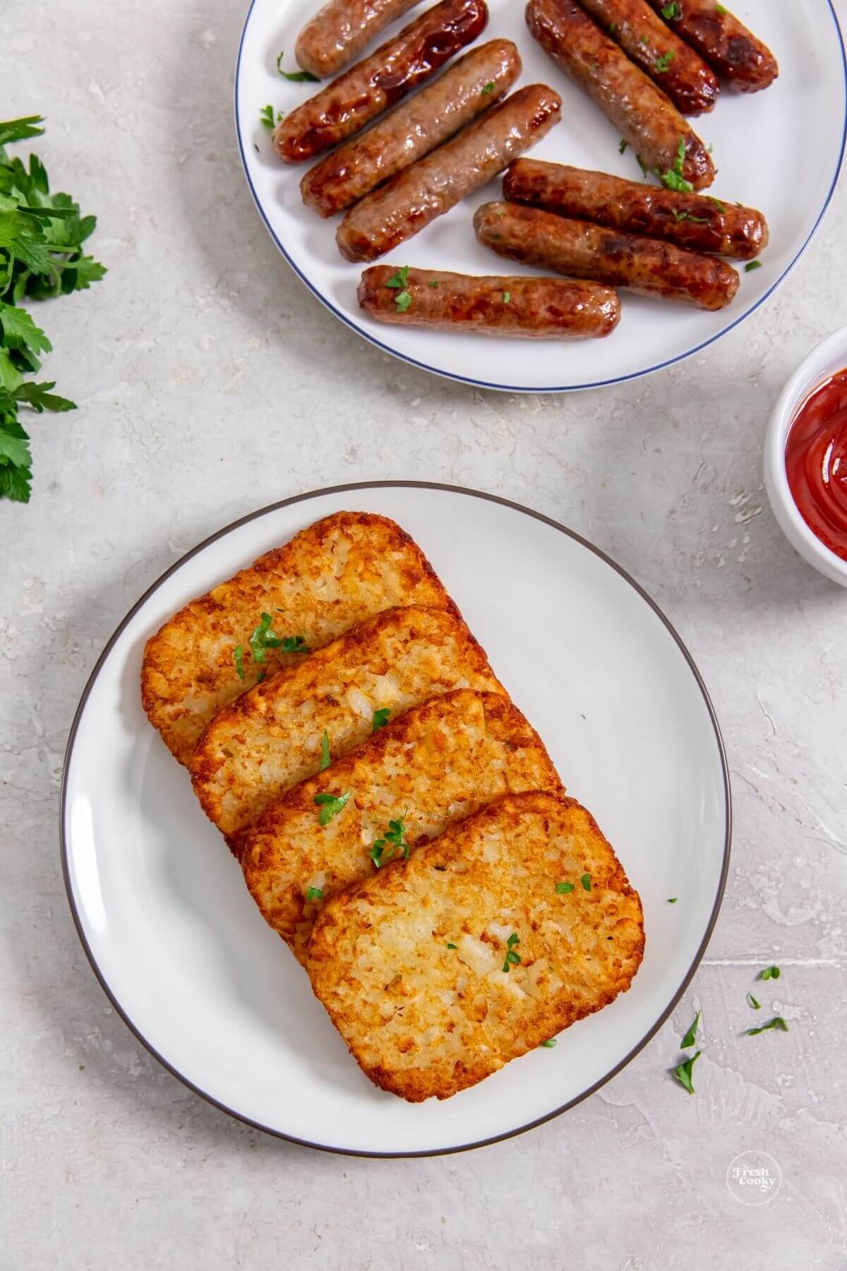 Air fryer frozen hash brown patties on plate with sausage links in background.