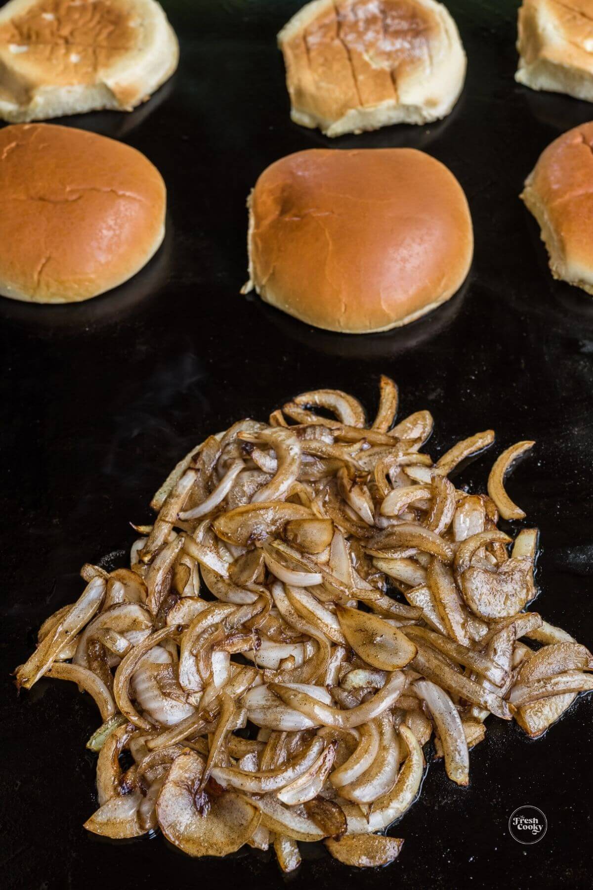 Grilling onions for smash burgers and toasting buttered buns in background.