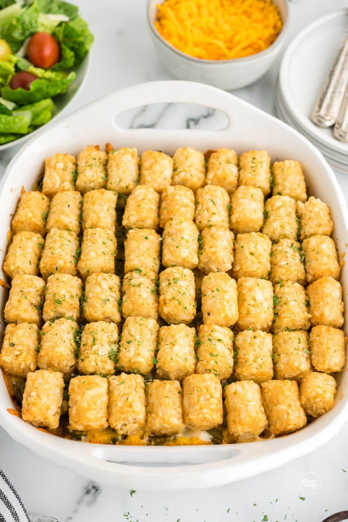 Tater tot casserole with salad in background, fresh from the oven.
