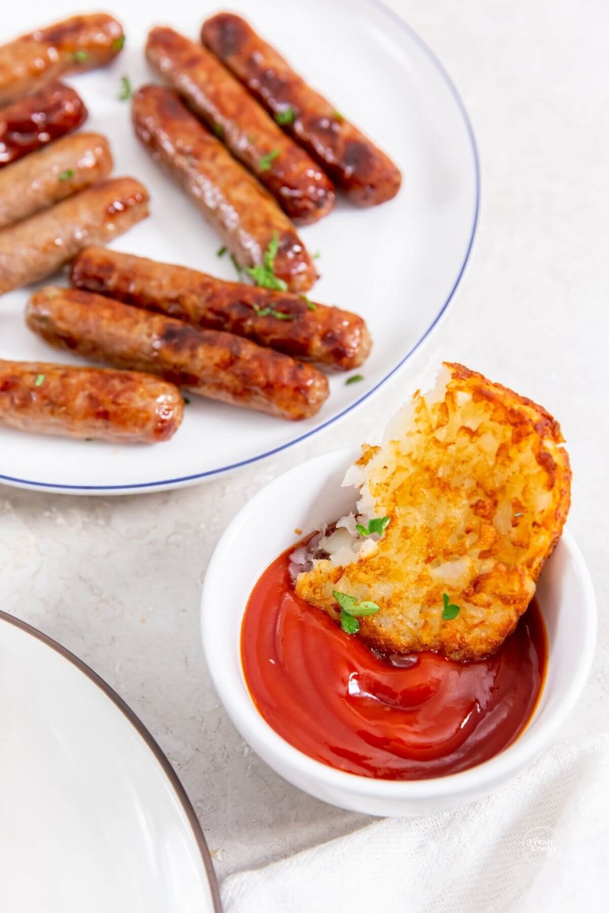 Half hash brown patty in ketchup with sausage links behind.