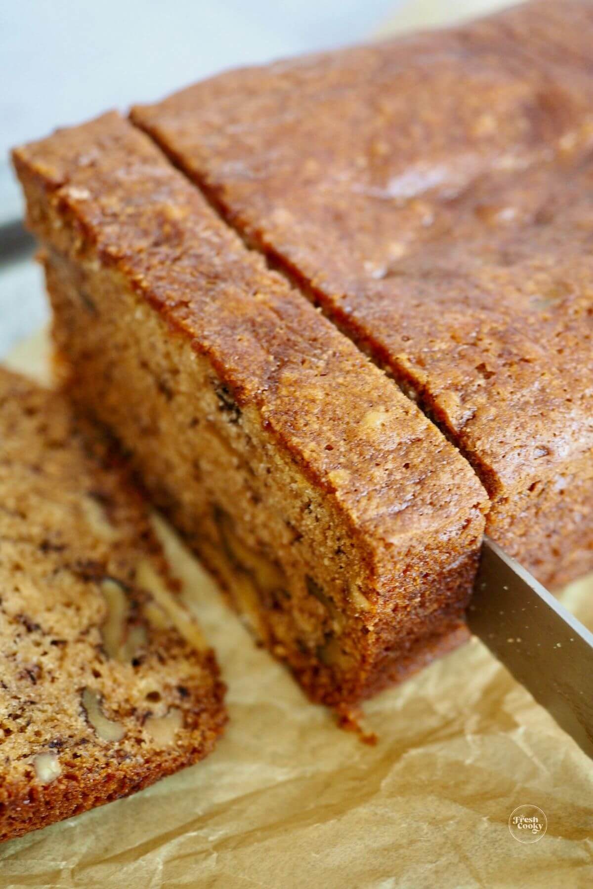 Slicing a thick slice of banana bread laced with walnuts.