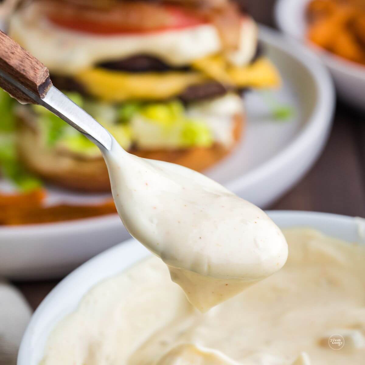 Easy smash burger sauce with spoon dipping in and cheeseburger with sauce in background.