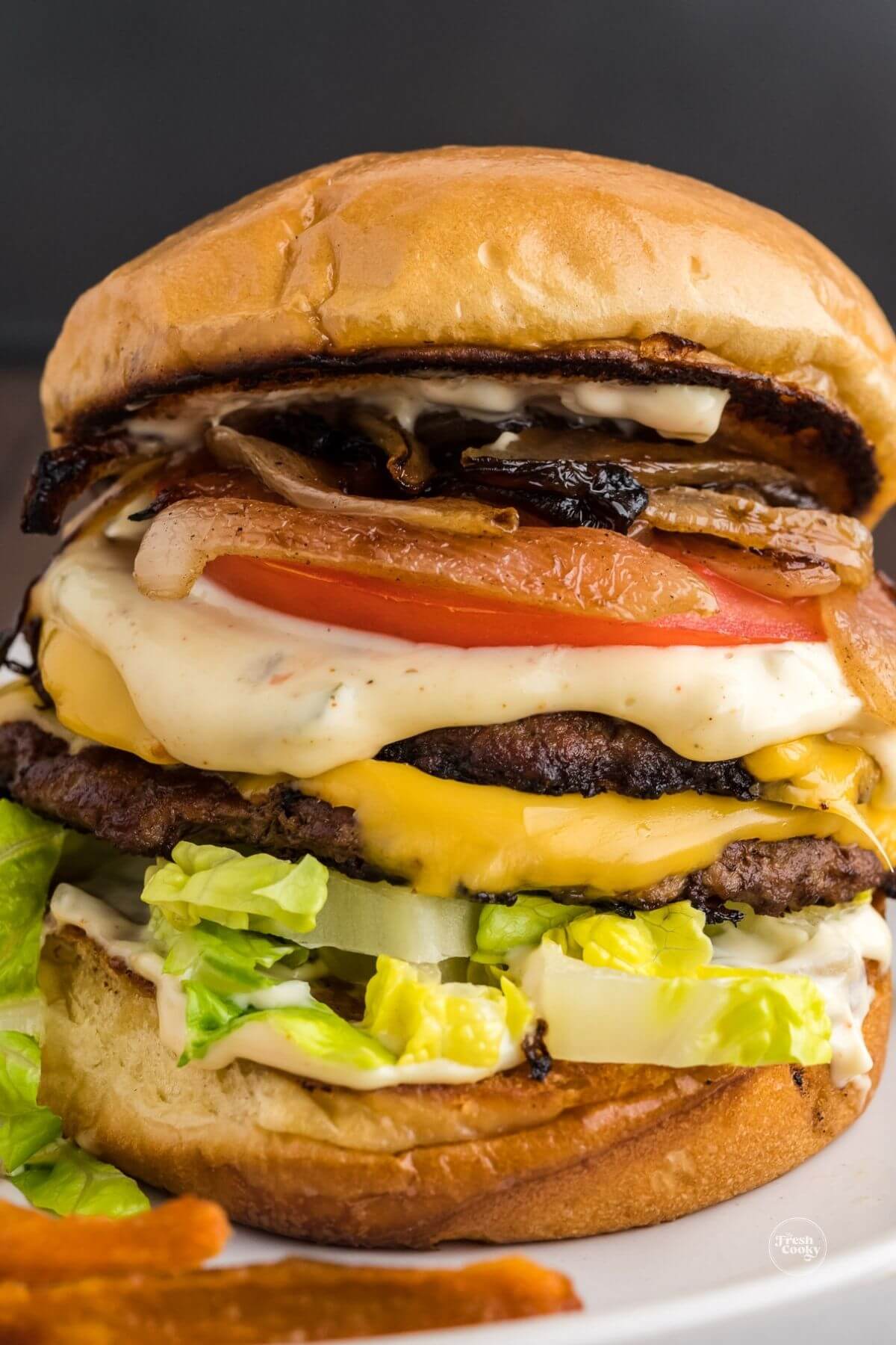 Close up of double smashburger with cheese, layered with grilled onions, smash sauce, lettuce and tomato.