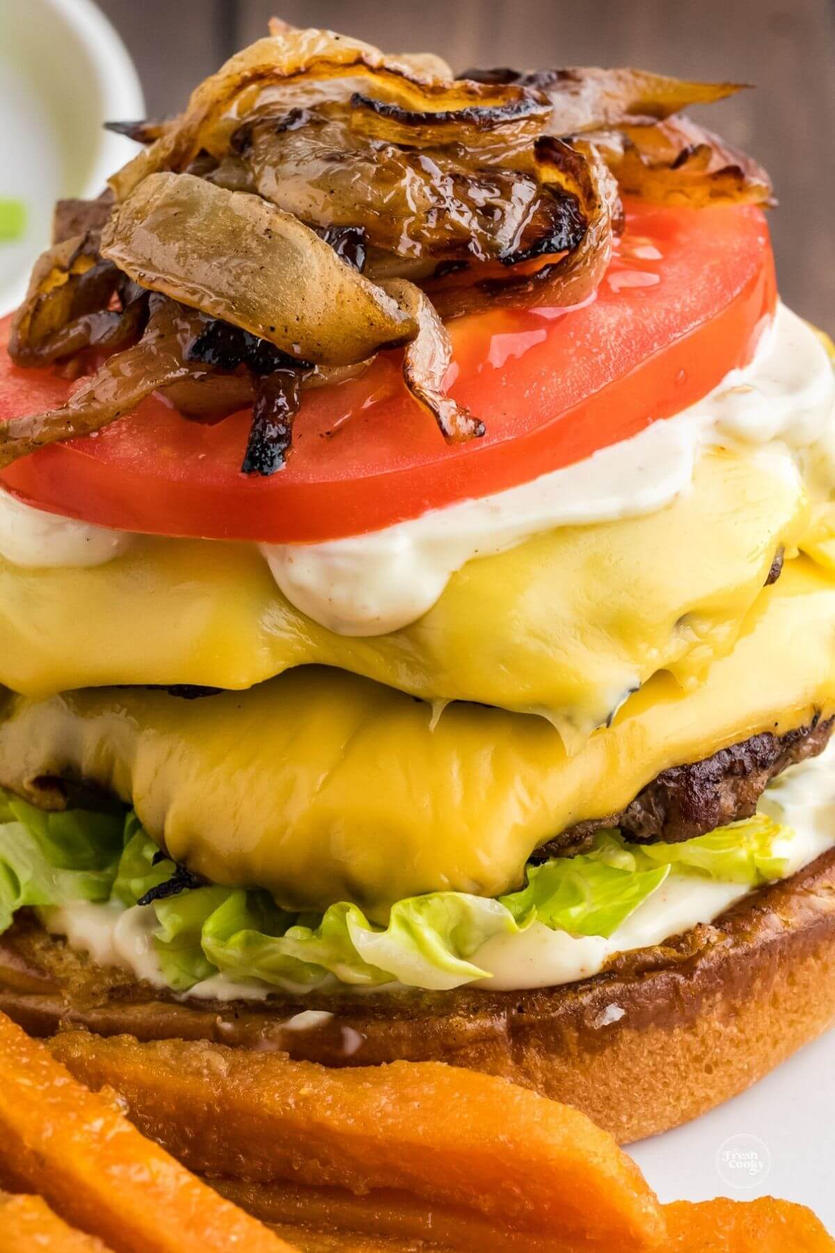 Loading up a smashburger with all the toppings and fixings, topping with tomato and grilled onions.