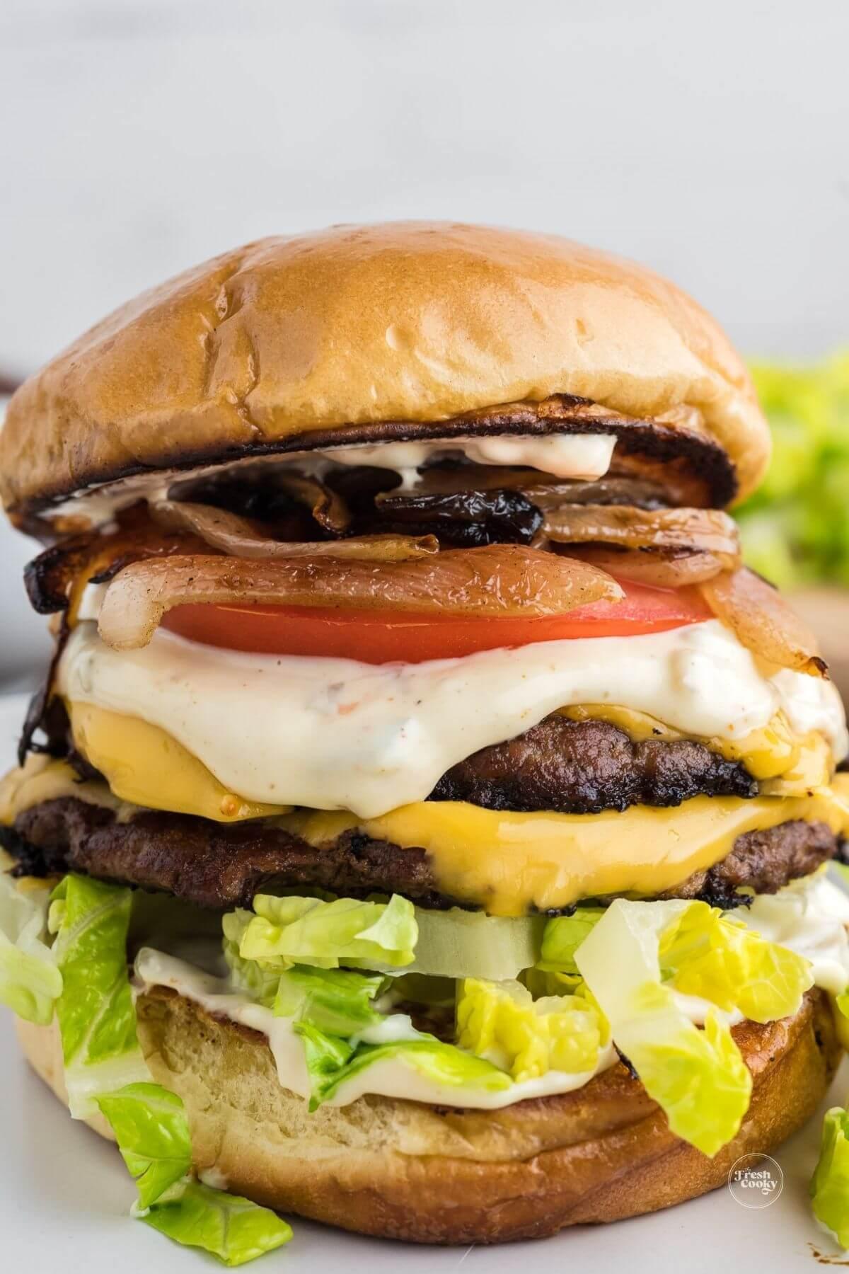 Stacked smashburger with layers of smash sauce, burgers, lettuce, tomatoes and grilled onions.