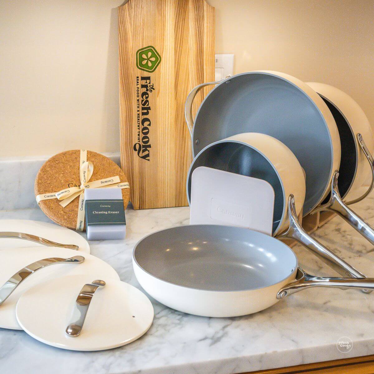 Caraway home cookware on display with magnetic holders, cork trivets and cleaning sponge.