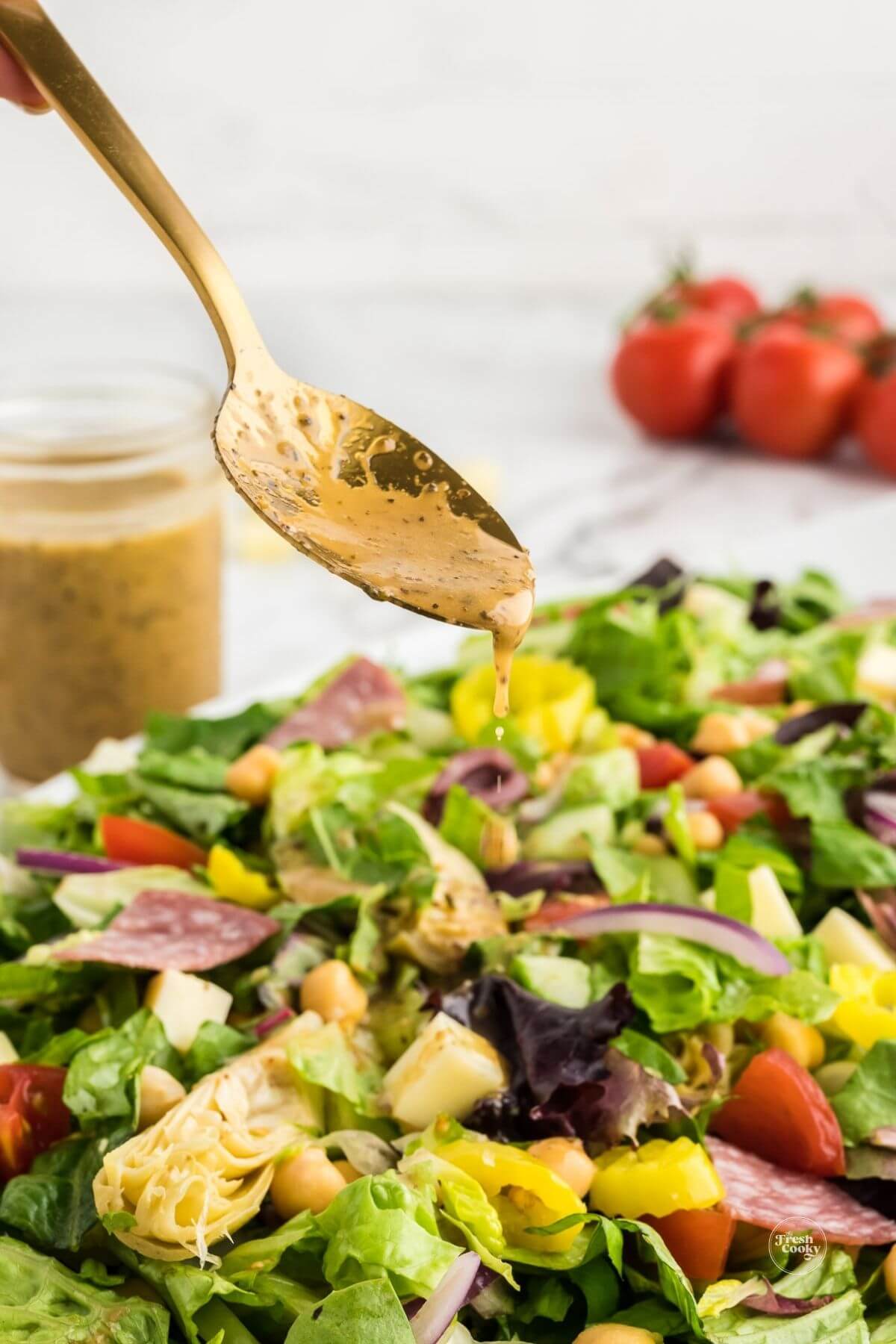 Spoon drizzling zesty Italian dressing onto chopped salad.