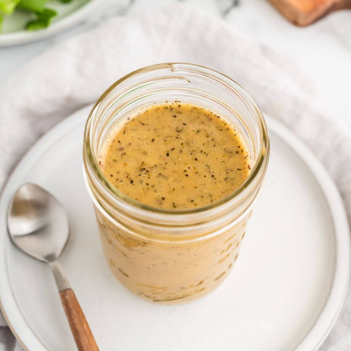 Jar filled with zesty Italian dressing recipe, on plate with spoon.