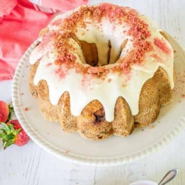 Gorgeous strawberry crunch pound bundt cake on pedestal, decorated with strawberry crunch topping and a sprinkle of strawberry powder.