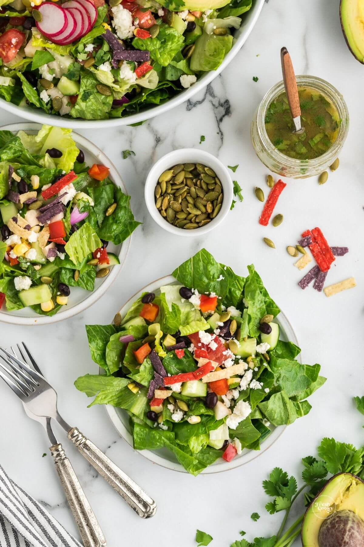 Servings of fresh and crunchy Mexican chopped salad in plates with salad bowl and dressing in a jar.