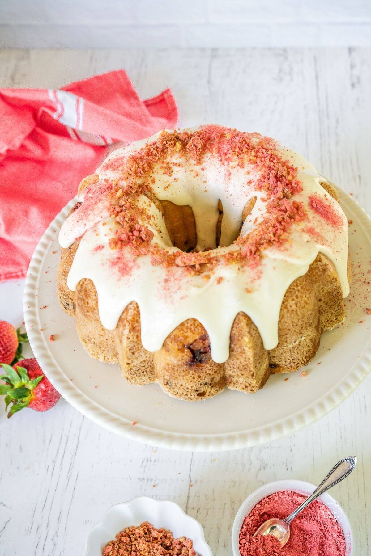 Gorgeous strawberry crunch pound bundt cake on pedestal, decorated with strawberry crunch topping and a sprinkle of strawberry powder.