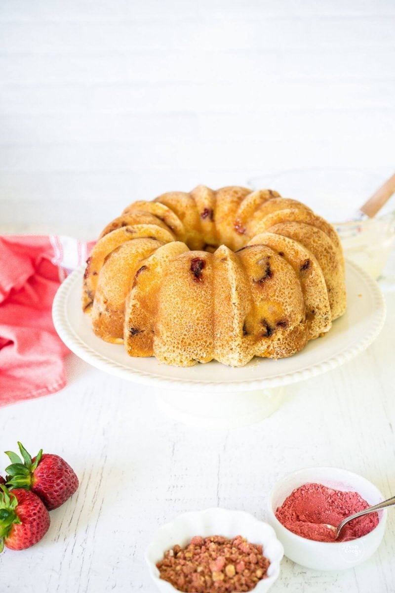 Strawberry bundt cake on pedestal with glaze behind.