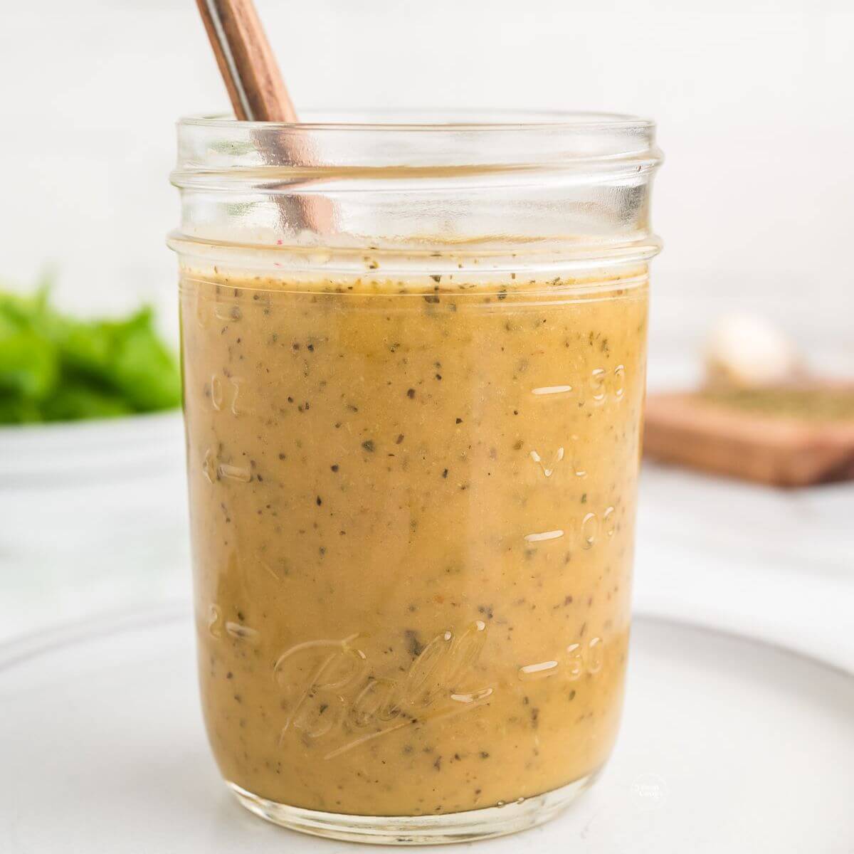 A jar filled with homemade zesty Italian dressing recipe with spoon.