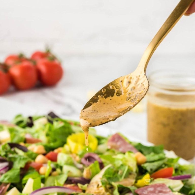 Spooning a zesty Italian dressing recipe onto a fresh green salad.