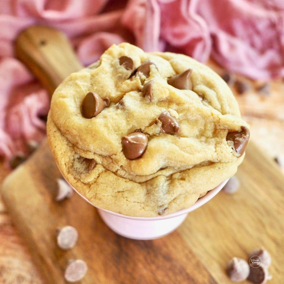 Copycat Crumbl Chocolate Chip Cookie on a pedestal with milk chocolate chips strewn about.