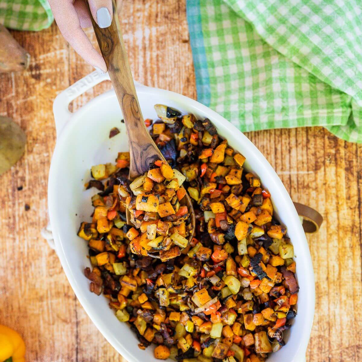 Diced potato hash browns in baking dish with wooden spoon.