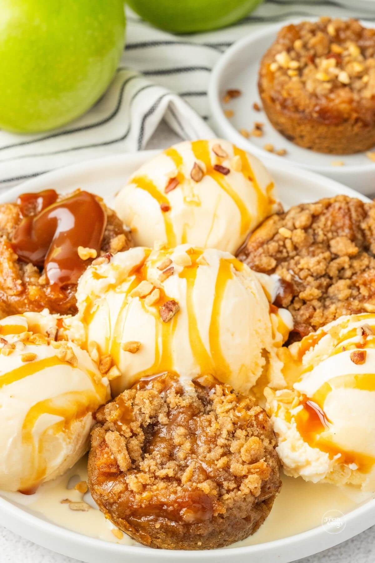 Mini apple pies on plate with vanilla ice cream, drizzled with caramel sauce.