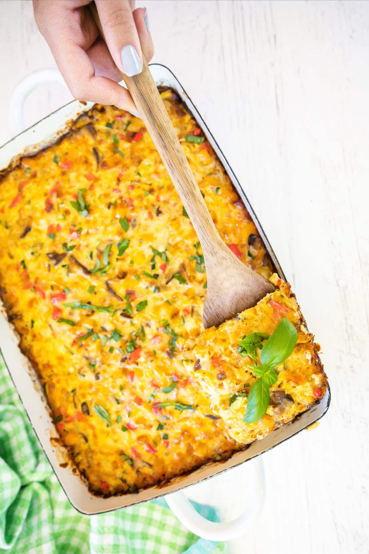 A hand serving a slice of vegetarian tater tot egg bake.