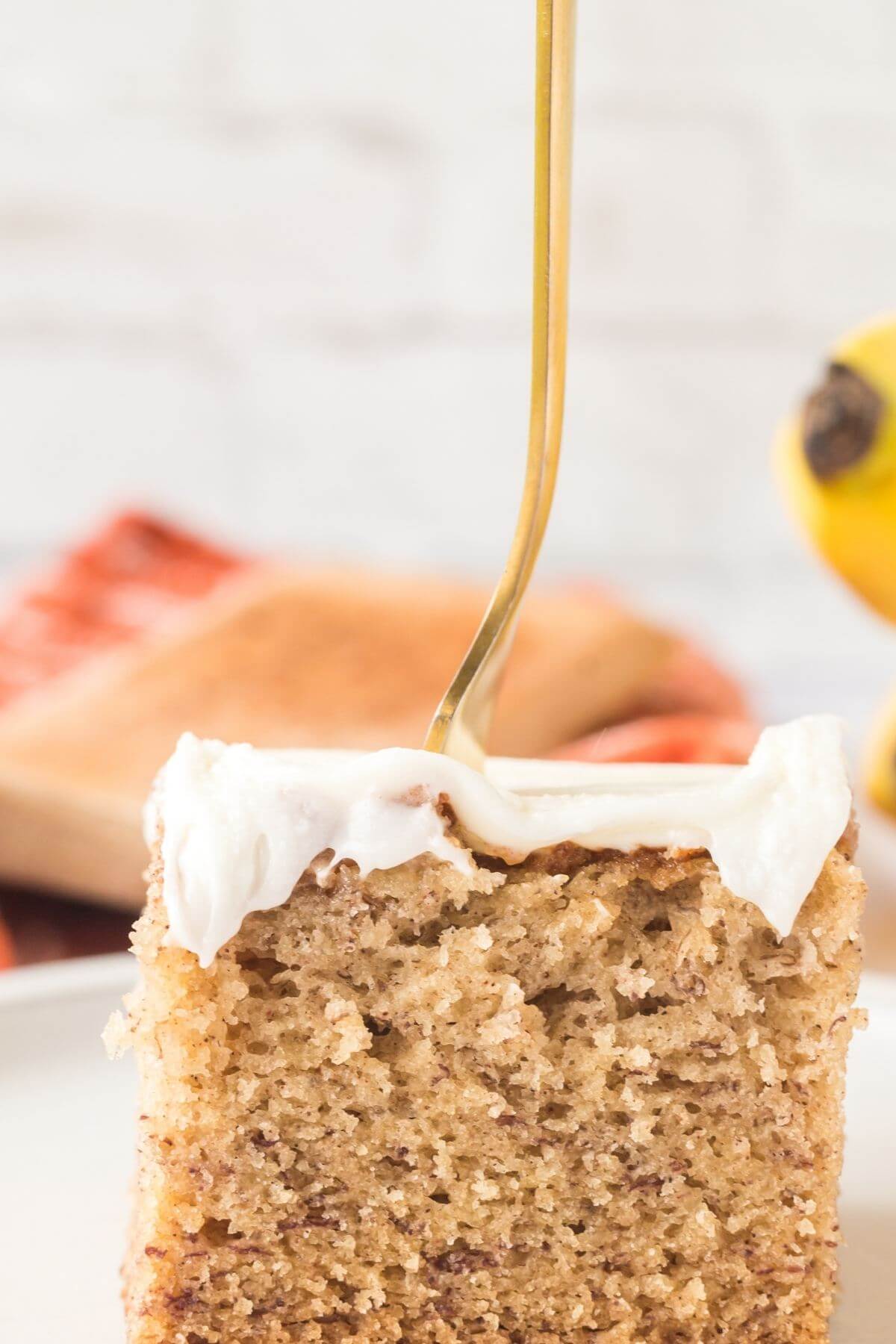 Gold fork stuck in center of slice of banana bars with cream cheese frosting.