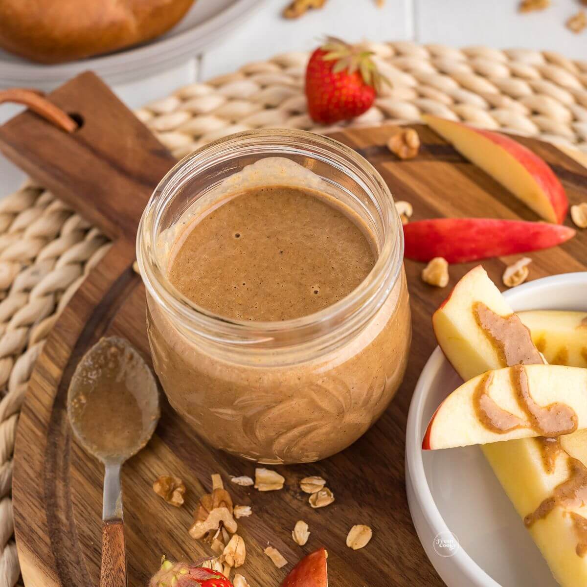 Granola butter in jar with apples and strawberries.