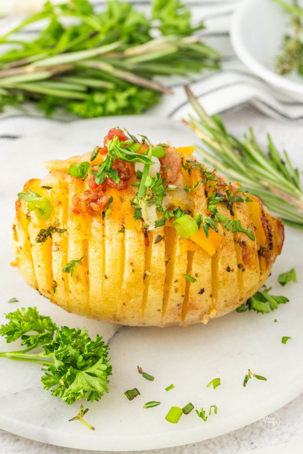 Hasselback potato in plate topped with a little shredded cheese, parsley and bacon bits.