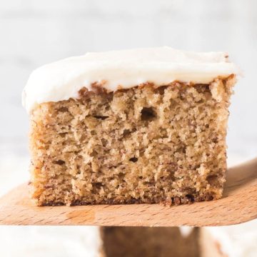 Best ever banana cake recipe on serving spatula, topped with cream cheese frosting.