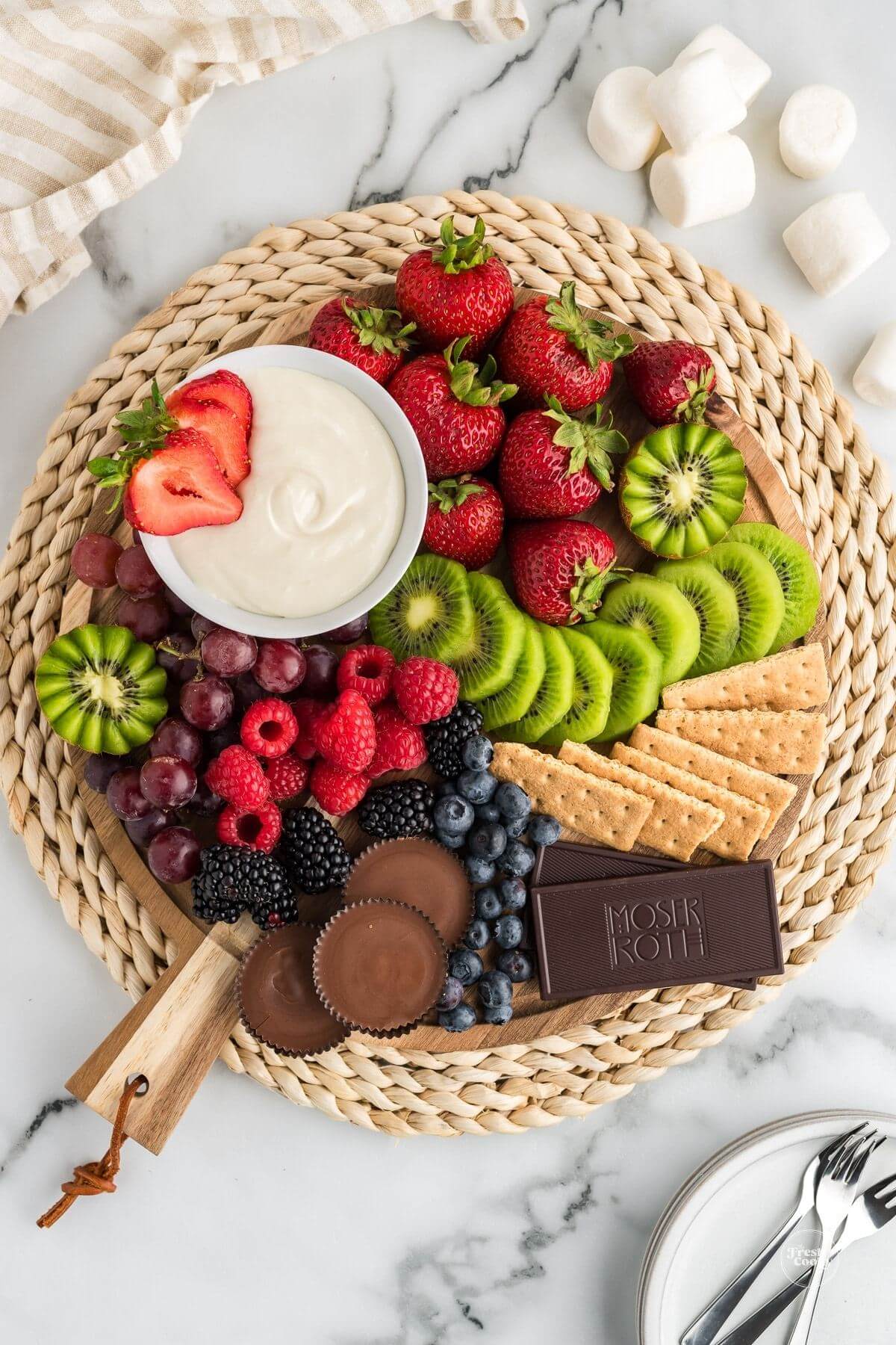 Platter with fresh fruits, crackers and chocolate surround a bowl of marshmallow fruit dip.
