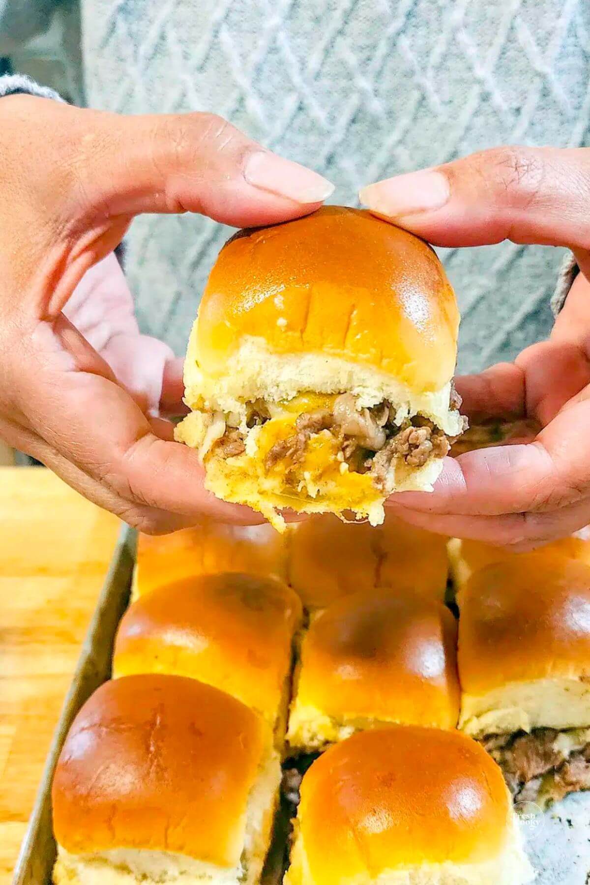 Beef and Cheddar sliders in hands ready to eat with melty cheese.