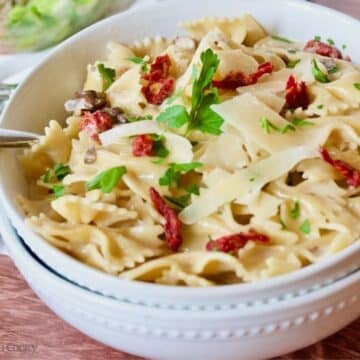 Two pasta bowls filled with creamy bow tied pasta with sun-dried tomatoes and shaved parmesan.
