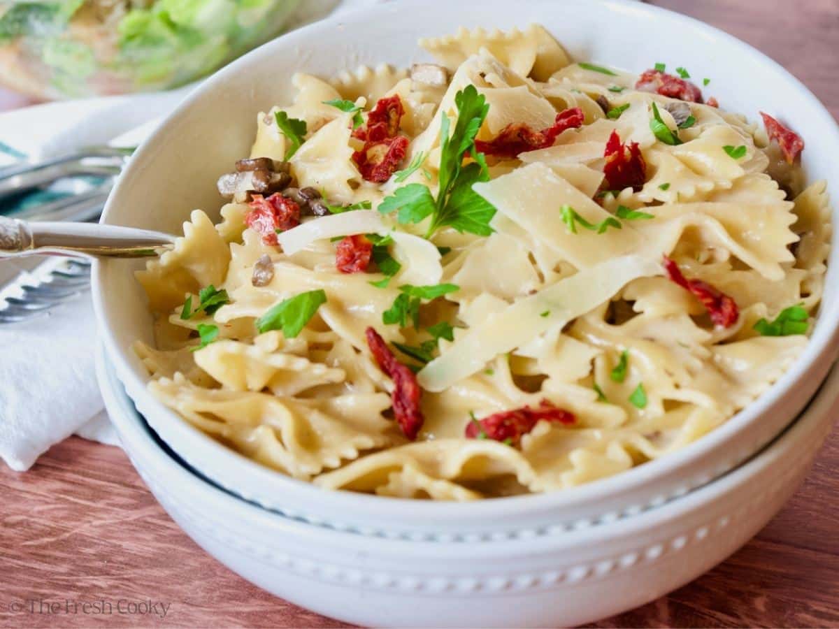 Two pasta bowls filled with creamy bow tied pasta with sun-dried tomatoes and shaved parmesan.