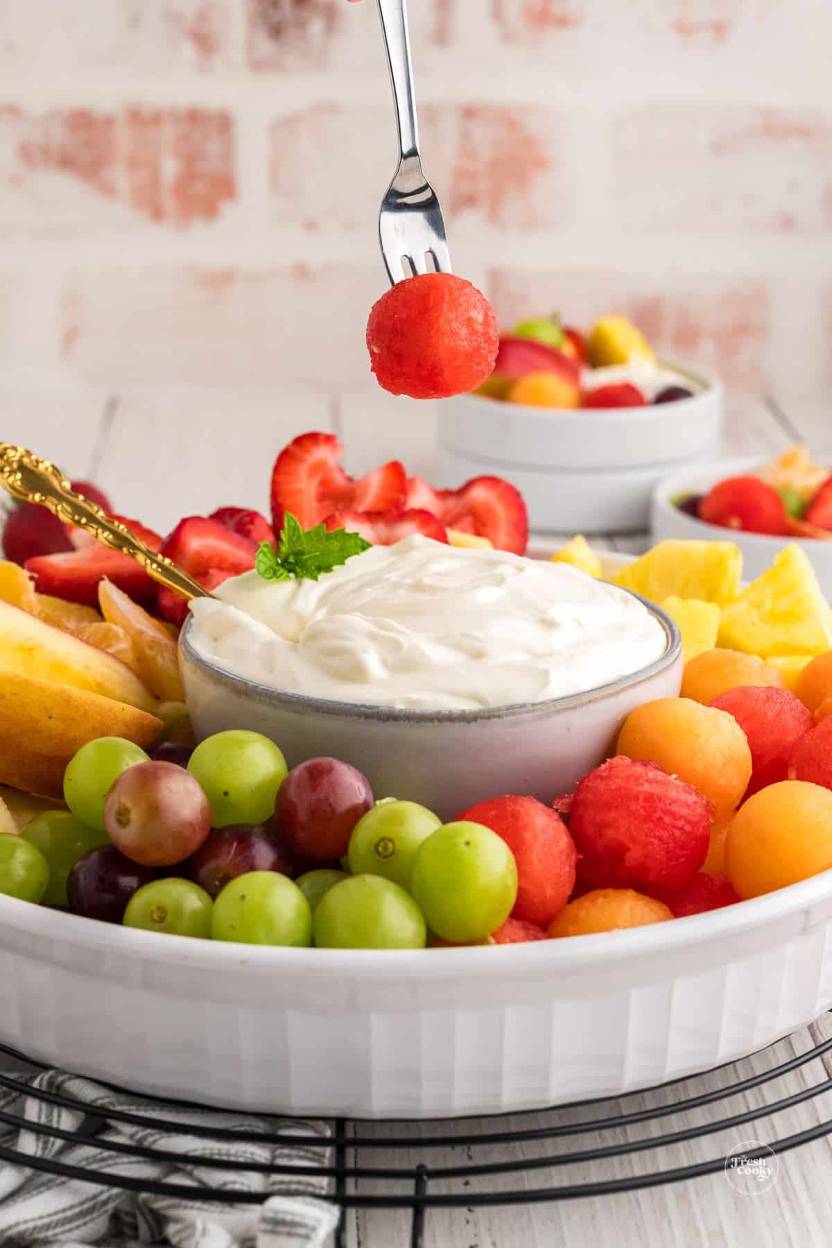 Fork dipping a watermelon ball into cream cheese fruit dip.