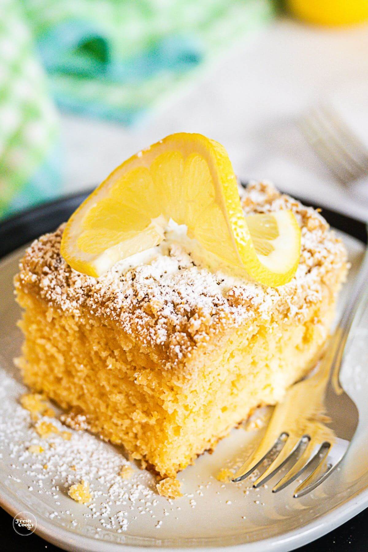 Large slice of lemon coffee cake with streusel topping and dusting of powdered sugar on plate.