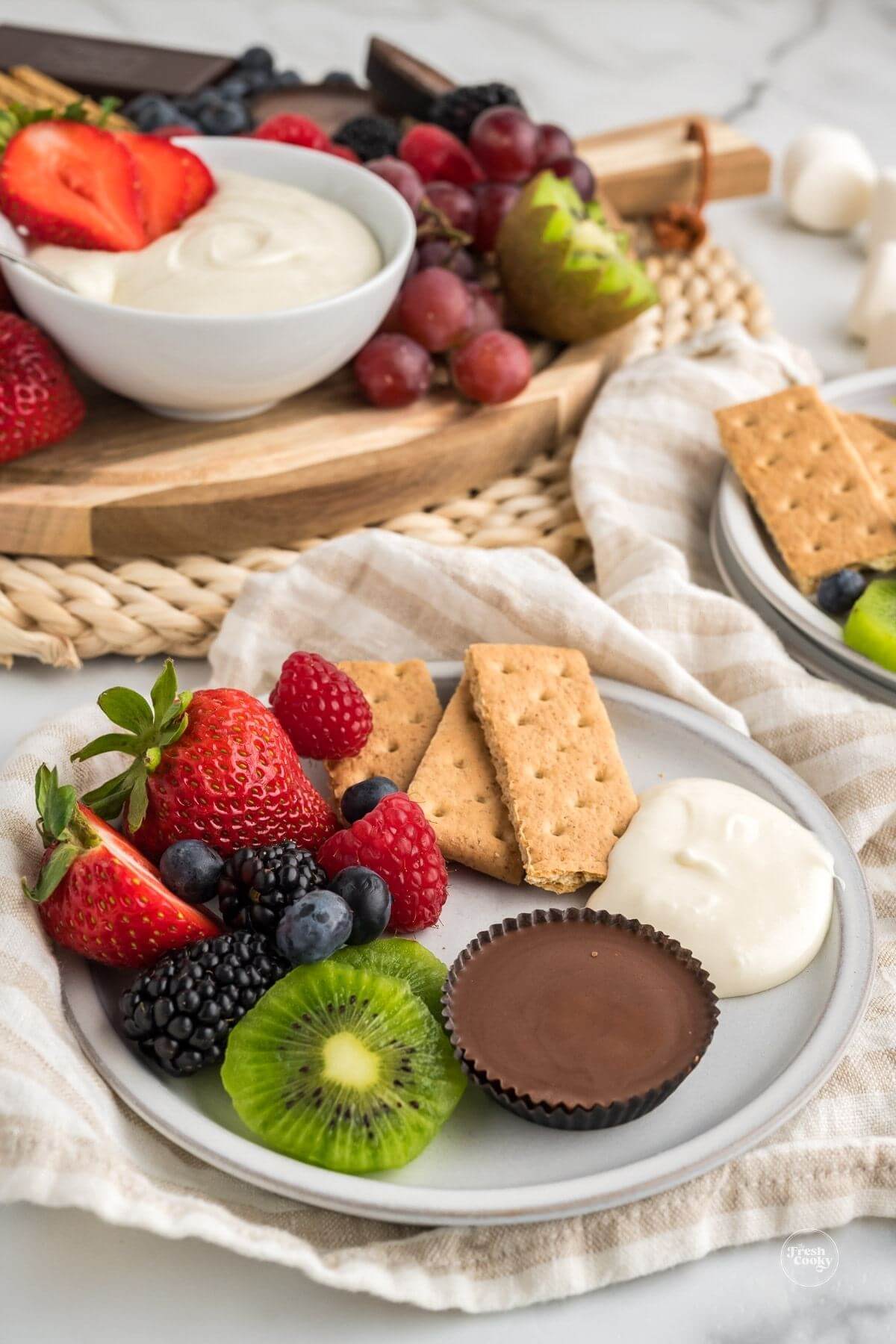 Fruit dip on plate with marshmallow dip in background.